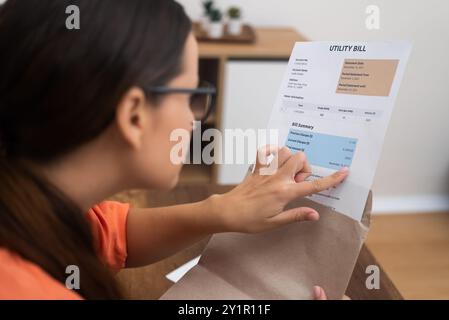 enveloppe à la main, une femme inspecte de près la facture de services publics, exposant de manière éclatante les taxes et les coûts du ménage Banque D'Images