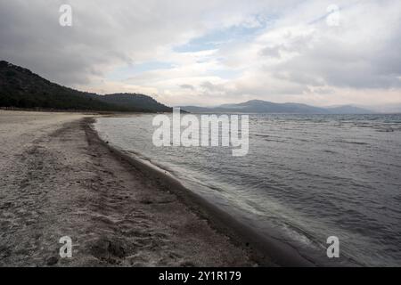 Une plage sereine s'étend le long du rivage du lac Salda, en Turquie. Le sable blanc immaculé contraste avec les eaux calmes et turquoises. Végétation luxuriante f Banque D'Images