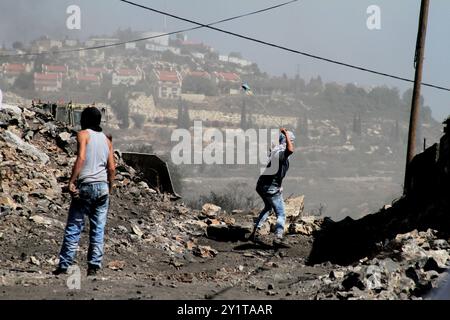 Un manifestant palestinien lance des pierres sur un véhicule militaire israélien lors d'affrontements à la suite d'une manifestation hebdomadaire contre l'expropriation de terres palestiniennes par Israël dans le village de Kfar Qaddum près de Naplouse, en Cisjordanie occupée. Banque D'Images