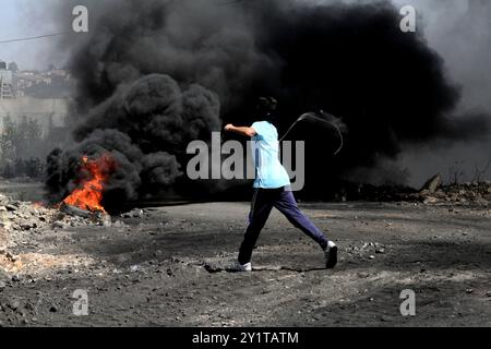 Un manifestant palestinien lance des pierres sur un véhicule militaire israélien lors d'affrontements à la suite d'une manifestation hebdomadaire contre l'expropriation de terres palestiniennes par Israël dans le village de Kfar Qaddum près de Naplouse, en Cisjordanie occupée. Banque D'Images