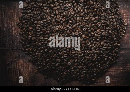 Une grande pile de grains de café est étalée sur une table en bois. La riche couleur brune des haricots contraste avec le grain naturel du bois Banque D'Images