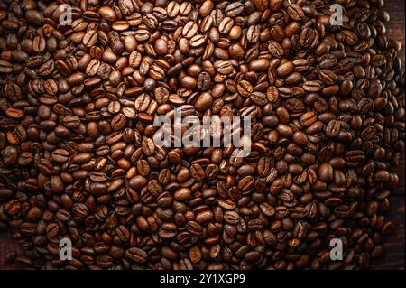 Une grande pile de grains de café est étalée sur une table en bois. La riche couleur brune des haricots contraste avec le grain naturel du bois Banque D'Images
