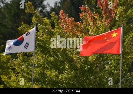 Les drapeaux nationaux de la Corée du Sud et de la Chine volent ensemble devant des feuilles vertes qui commencent à tourner aux couleurs à l'automne. Banque D'Images