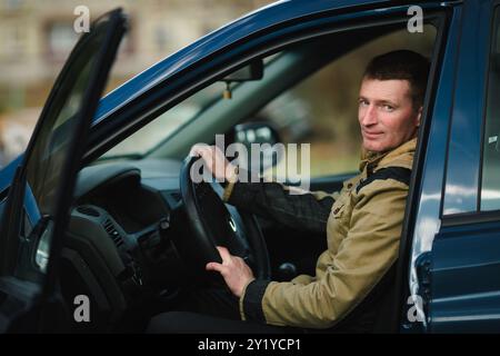 Portrait d'un homme assis au volant de sa voiture, regardant la caméra avec confiance. L'intérieur du véhicule est visible, à la lumière naturelle Banque D'Images