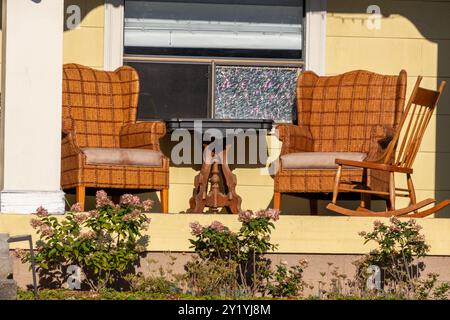 Le soleil brille sur des chaises en osier et une chaise à bascule à l'ancienne sur un porche Banque D'Images