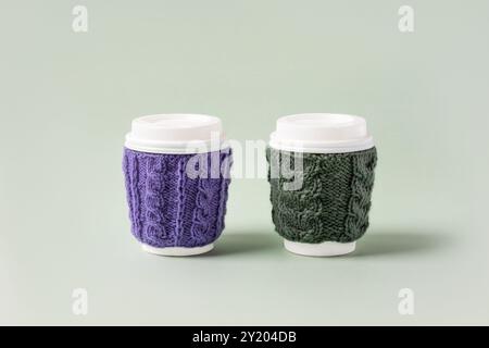 Deux tasses en carton pour le café à emporter avec couvercle tricoté vert et violet et couvercle bioplastique blanc. Concept de café à emporter, marche, vie énergique Banque D'Images