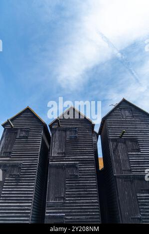 Trois hangars de séchage de filets de pêche noirs à Rock-a-Nore, Hastings par une journée ensoleillée avec un ciel bleu et des nuages blancs tortueux Banque D'Images