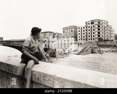 1945 , 26 avril , VÉRONE , VÉNÉTIE , ITALIE : DE LA LÉGENDE ORIGINALE : ' Cinquième armée américaine à Vérone . Garçon italien regarde sur la rivière Adige et le pont della Vittoria que les Allemands nazis et fascistes italiens dynamités lors de l'évasion '. Dans la nuit du 25 avril 1945, quand il a été miné et explosé par des soldats allemands en retraite, une explosion qui a laissé intacte seulement l'arche vers la ville. Sur cette photo prise depuis Lungadige Panvinio, vous pouvez également voir la dévastation de toutes les maisons face au pont surplombant Lungadige Giamomo Matteotti ( comme aujourd'hui renommé ) et le camp de Lungadige Banque D'Images