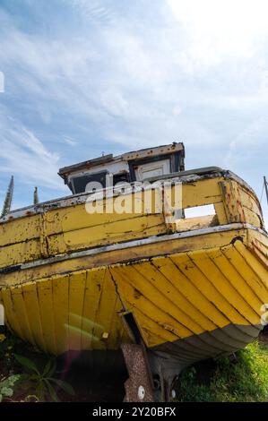 Vieux, jaune pâle, bateau de pêche en clinker en bois sur le rivage à Hastings, par une journée ensoleillée avec des raccords rouillés, à la poupe Banque D'Images