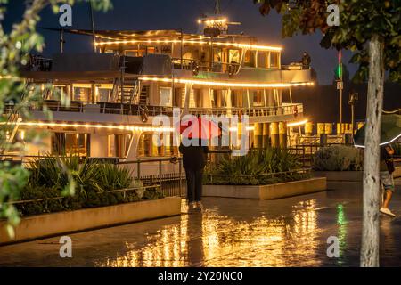 Wetterwechsel am Bodensee, Passagierschiff legt abends BEI Starkregen in Überlingen an, der Herbst naht, 8. Septembre 2024 Deutschland, Überlingen, 8. Septembre 2024, Wetterwechsel am Bodensee, eine Regenfront mit Starkregen Hat am Sonntag das schöne Sommerwetter abgelöst, der Herbst ist da, das Passagierschiff Stuttgart legt abends um 20 Uhr in Überlingen an, Frau mit rotem Regenschirm steht an der Uferpromenade, die Lichter des Schiffs spiegeln sich im nassen Asphalt, Touristen, Urlaubszeit, Schifffalotte, Weiße, Schifffalotte BSB, Spätsommer, Bade-Württemberg, *** changement de temps sur le lac de Constance, Banque D'Images