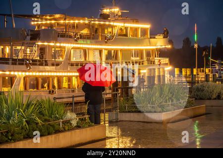 Wetterwechsel am Bodensee, Passagierschiff legt abends BEI Starkregen in Überlingen an, septembre 2024 Deutschland, Überlingen, 8. Septembre 2024, Wetterwechsel am Bodensee, eine Regenfront mit Starkregen Hat am Sonntag das schöne Sommerwetter abgelöst, der Herbst ist da, das Passagierschiff Stuttgart legt abends um 20 Uhr in Überlingen an, Frau mit rotem Regenschirm steht an der Uferpromenade, die Lichter des Schiffs spiegeln sich im nassen Asphalt, Touristen, Urlaubszeit, Schifffalotte, Weiße, Schifffalotte BSB, Spätsommer, Bade-Württemberg, *** changement de temps sur le lac de Constance, quais de navires à passagers Banque D'Images