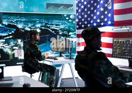 Officier militaire AMÉRICAIN supervisant l'activité de détection des menaces dans le bureau de haute technologie, examinant les données top secrètes sur grand écran. Soldats de l'armée américaine gérant la guerre hybride, prévention des cyberattaques. Banque D'Images