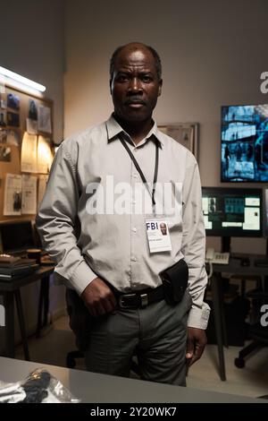 Enquêteur détective dans un bureau de surveillance bien équipé avec plusieurs moniteurs, travaillant sur des preuves et des dossiers de différents cas. Porter un badge d'identification officiel et un étui à pistolet Banque D'Images