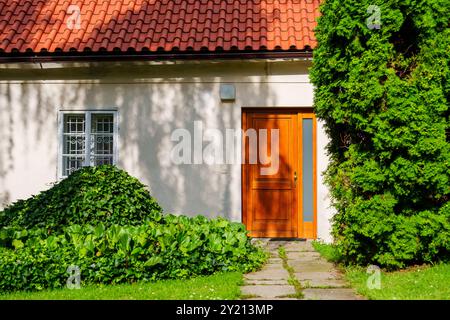 Charmante maison de banlieue avec une porte brune, un toit rouge et un beau jardin de fleurs en pleine floraison Banque D'Images