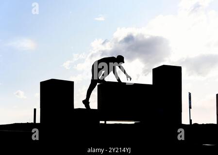 Silhouette rétro-éclairée d'un homme actif grimpant sur des blocs de béton pratiquant le parkour, un sport urbain athlétique populaire parmi les jeunes. Banque D'Images