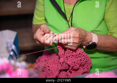Mains de femme âgée tricotant, gros plan, fil rose, activité artisanale, vue détaillée, confortable, compétence traditionnelle, chemise verte, senior, temps de loisirs, ho Banque D'Images