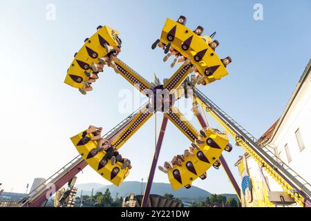 Tour passionnant de parc d'attractions mettant en vedette des gens joyeux, structure jaune vibrante, lumière du jour brillante, plaisir en plein air, concept d'expérience palpitante Banque D'Images