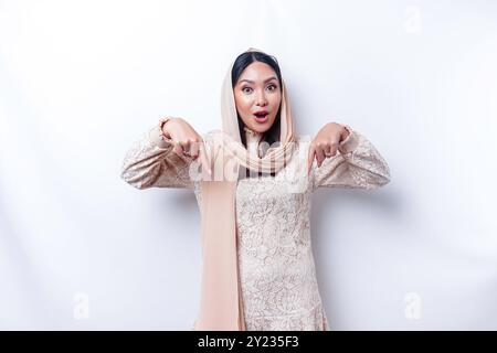 Femme musulmane asiatique choquée portant le hijab pointant vers l'espace de copie en dessous d'elle, isolée par fond blanc. Banque D'Images