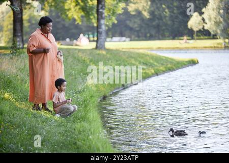 Afro-américain Branny et son charmant petit-fils nourrissant les canards avec du pain blanc dans le parc vert Banque D'Images