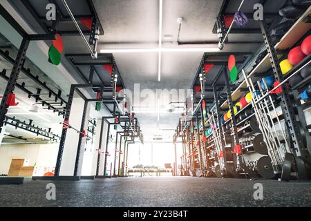 Vue en angle bas des rangées d'équipements de gymnastique, balles de médecine en caoutchouc, dubbells et kettlebells sur des supports pour la musculation dans le gymnase. Banque D'Images