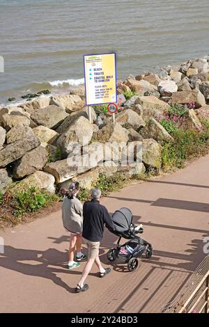 Maman papa landaus & bébé Sunshine Walk le long de South West Coast Path entre les rochers de défense maritime et Riviera Line Railway Dawlish Devon Angleterre Banque D'Images