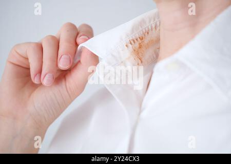 Femme sans visage montrant une tache cosmétique sale sur le col de sa chemise blanche dans une pièce bien éclairée pendant la journée. concept de coloration de la vie quotidienne. . Élevé Banque D'Images