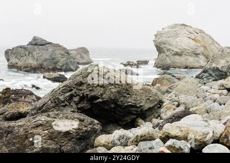 De grands rochers le long d'une côte brumeuse avec des vagues et un ciel couvert Banque D'Images