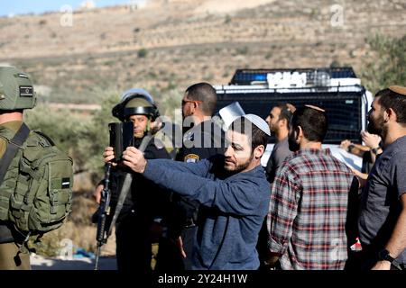 Naplouse, Cisjordanie, Palestine. 28 novembre 2021. Des colons juifs israéliens se rassemblent aux côtés de soldats israéliens dans le village palestinien de Lubban Ash-Sharqiya, au sud de Naplouse. Les colons étaient entrés dans le village alors que certains de ses habitants se rassemblaient pour protester contre les récentes attaques quotidiennes des colons à l’école de Lubban Ash-Sharqiya pour empêcher les élèves d’accéder à l’école et à leurs cours. Les colonies judéo-israéliennes continuent de s'étendre en Cisjordanie et à Jérusalem-est, bien qu'elles constituent une violation du droit international Banque D'Images