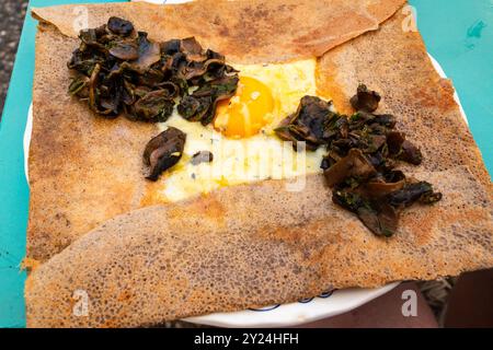 Galette salée (crêpe française à base de farine de sarrasin) avec œuf de champignons frits et fromage servi pour le déjeuner dans un bistrot français Banque D'Images