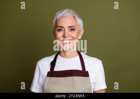 Photo de brillant tablier habillé de dame attrayant préparant des boissons souriant espace vide isolé fond de couleur verte Banque D'Images