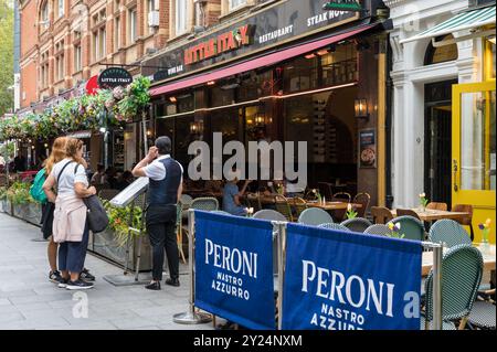 Deux femmes en conversation avec le serveur maître d' au tableau de menu devant Little Italy restaurant italien Irving Street Leicester Square Londres Angleterre Royaume-Uni Banque D'Images