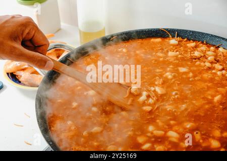 gros plan d'un homme remuant la poêle à paella où est la cuisson d'une fideua espagnole dans une cuisine domestique Banque D'Images