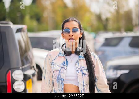 Femme indienne dans une tenue en denim élégante avec une valise rose, voyageant à l'aéroport en voiture et en bus, vérifiant son téléphone en attendant. Banque D'Images