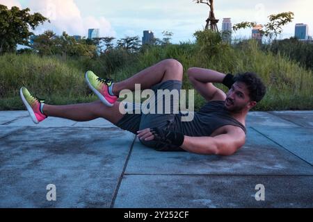 Homme travaillant dans un parc dans le centre de Bangkok, faisant une routine abs sur le sol avec les gratte-ciel de Bangkok en arrière-plan Banque D'Images