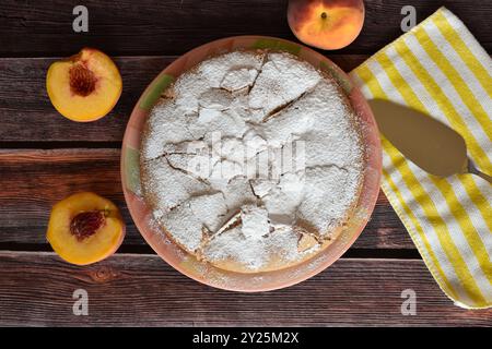 Tarte charlotte maison fraîchement cuite avec des pêches sur une table en bois. Gâteau saupoudré de sucre en poudre, pelle à gâteau en métal sur serviette rayée. Vue de dessus. Banque D'Images