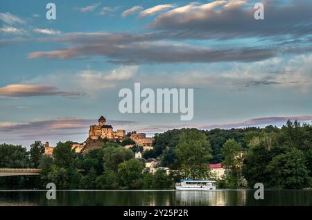 Ville Trencin avec la rivière Vah, bateau flottant et un château en arrière-plan au coucher du soleil. Nuages roses dans le ciel bleu foncé. Paysage d'été. Slovaquie Banque D'Images