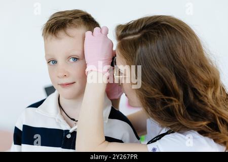 Médecin féminin examinant l'oreille d'un garçon à l'otoscope en cabinet. Bilan de santé du traitement de la cavité auditive. Banque D'Images