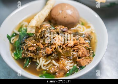 Un bol de nouilles garni de boulettes de viande, de viande râpée et de légumes-feuilles, servi avec des craquelins croustillants sur le côté. Banque D'Images