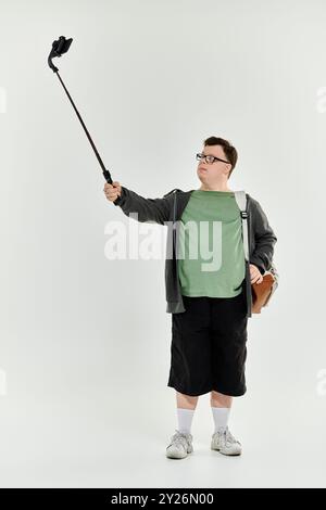 Un jeune homme atteint du syndrome de Down se tient confiant en prenant un selfie avec un bâton. Banque D'Images