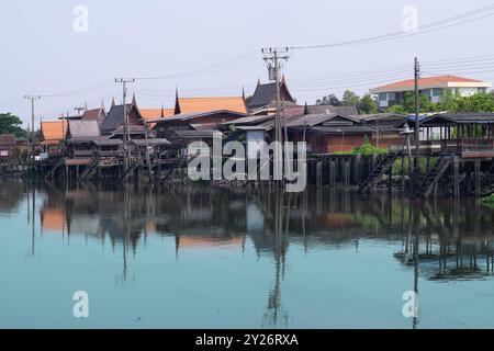 Une vue sereine sur les maisons thaïlandaises traditionnelles construites sur pilotis colonne le long du bord d'une rivière calme. Les structures en bois, avec leur roo pointue distincte Banque D'Images