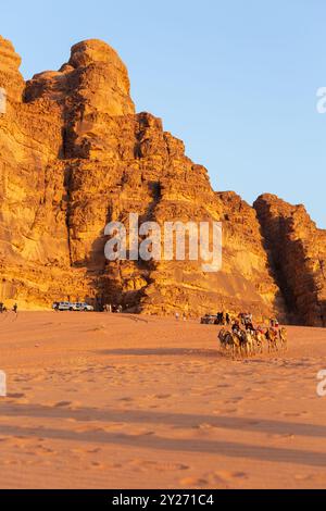 Jordanie, Wadi Rum - 2 novembre 2022 : caravane de chameaux avec chauffeurs dans le désert, montagnes rocheuses au coucher du soleil Banque D'Images