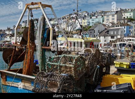 Homard pots et filets à l'arrière d'Un chalutier de pêche amarré dans le port de Brixham avec Quay et maisons en arrière-plan, Royaume-Uni Banque D'Images