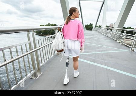 Une jeune femme en vêtements de sport profite d'une journée à l'extérieur tout en marchant en toute confiance sur un pont. Banque D'Images