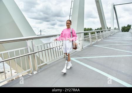 Une jeune femme animée en vêtements de sport traverse en toute confiance un pont moderne, profitant de sa journée à l'extérieur. Banque D'Images