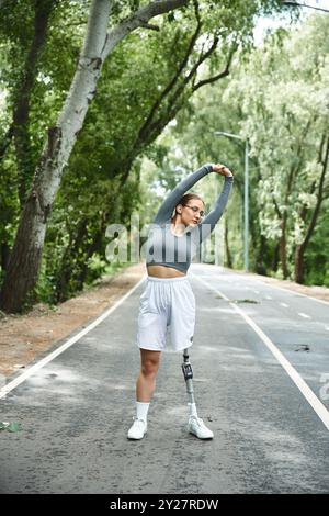 Une jeune femme profite d'une journée ensoleillée à l'extérieur, s'étirant et faisant de l'exercice en vêtements de sport avec une jambe prothétique. Banque D'Images