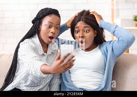 Choqué Black Girls Looking At Smartphone la lecture à l'écran Message inattendu Banque D'Images