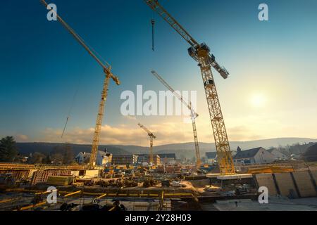 Grand chantier de construction avec quatre grues jaunes se projetant dans le ciel bleu avec le soleil et les nuages. Vue grand angle inclinée vers le haut. Banque D'Images