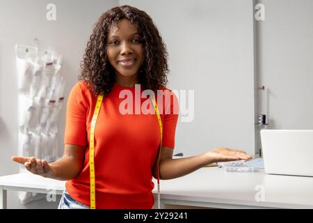 Femme tailleur en T-shirt orange posant dans l'espace de travail de sa couturière créative Banque D'Images