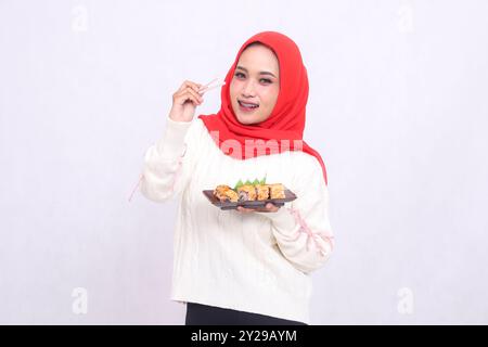 Fille indonésienne portant un hijab est heureuse de voir le devant ramasser avec des baguettes et portant une assiette contenant des sushis (nourriture japonaise). Beau M Banque D'Images