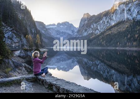 Une femme faisant du yoga (Gomukhasana, Garudasana) au bord du lac. Vorderer Gosausee en automne avec vue sur les montagnes de Dachstein. Le Gosaukamm sur la plate-forme Banque D'Images